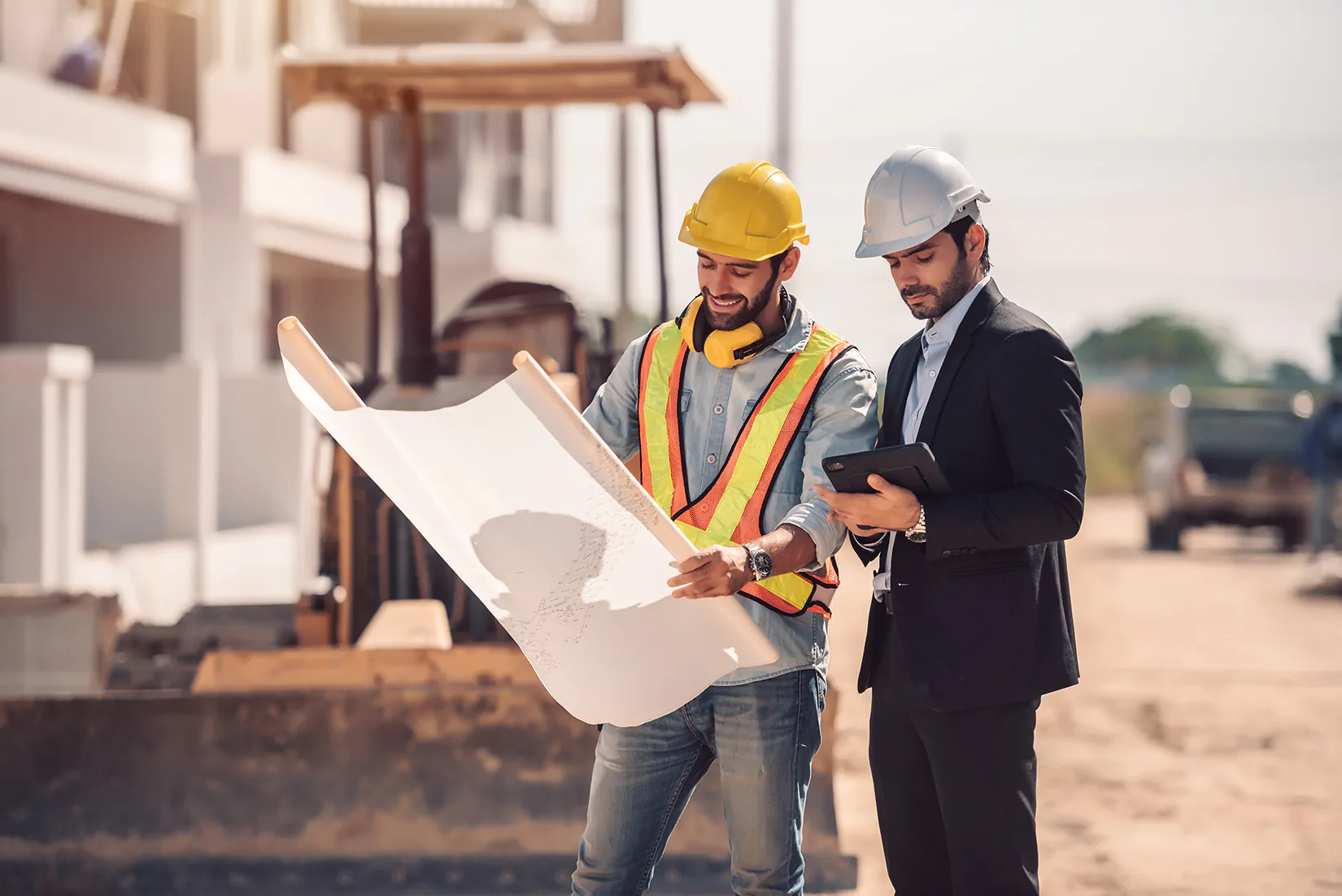 Engenheiro de construção civil com tablet e plantas analisando projeto em canteiro de obra